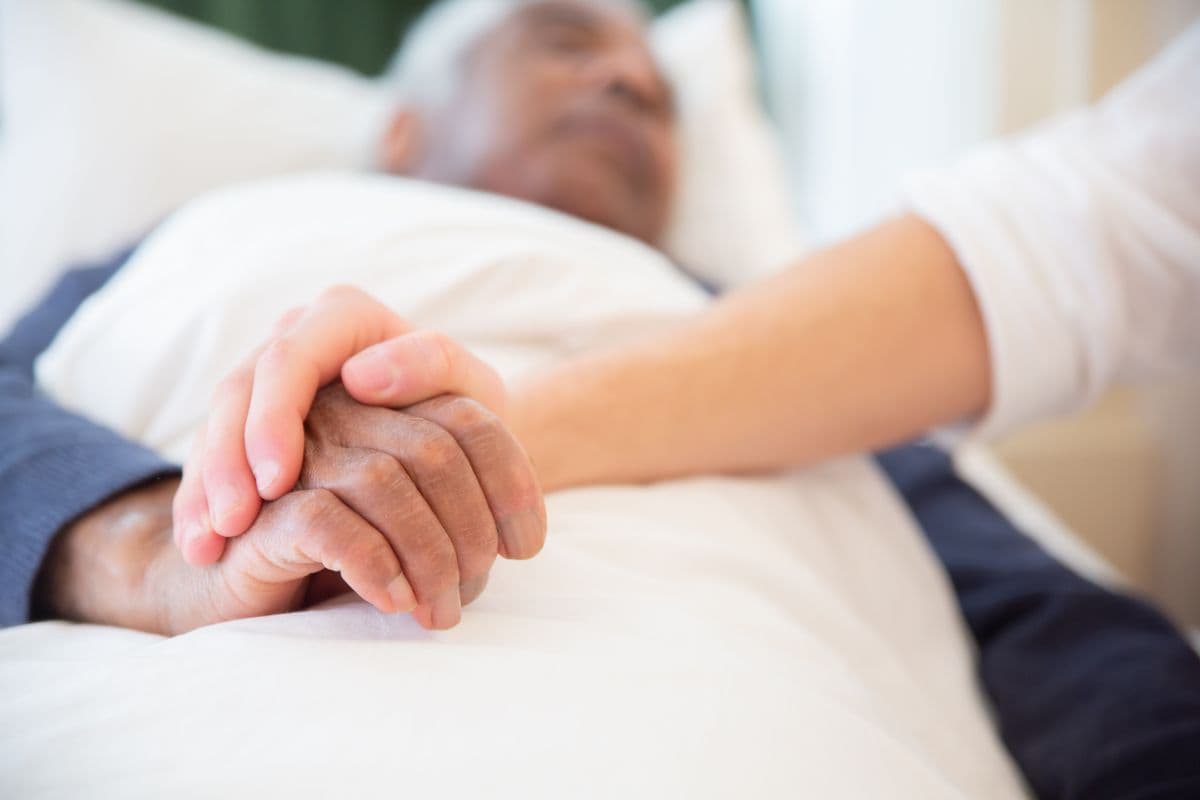 A caregiver gently holding a senior client's hand